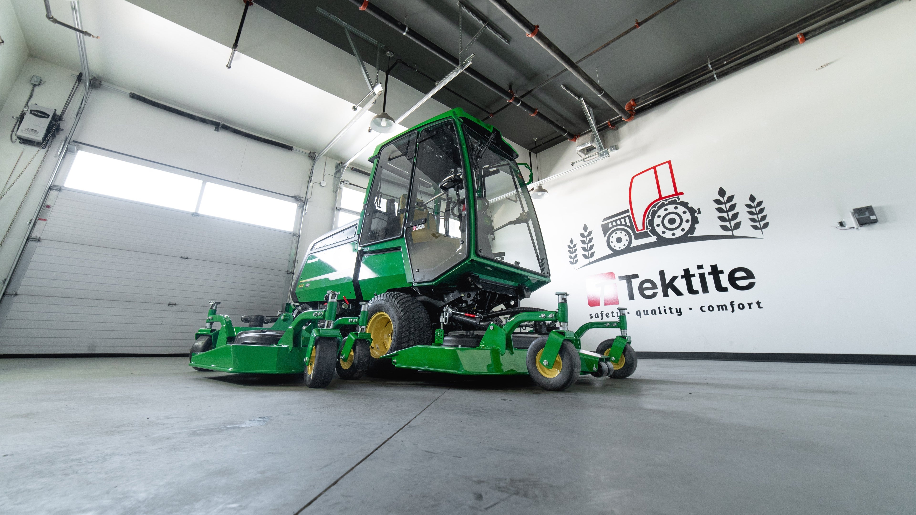 Green industrial vehicle in a large indoor facility with Tektite branding on the wall.